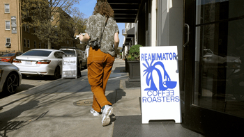 A woman walks past a Reanimator Coffee & Roasters sign.